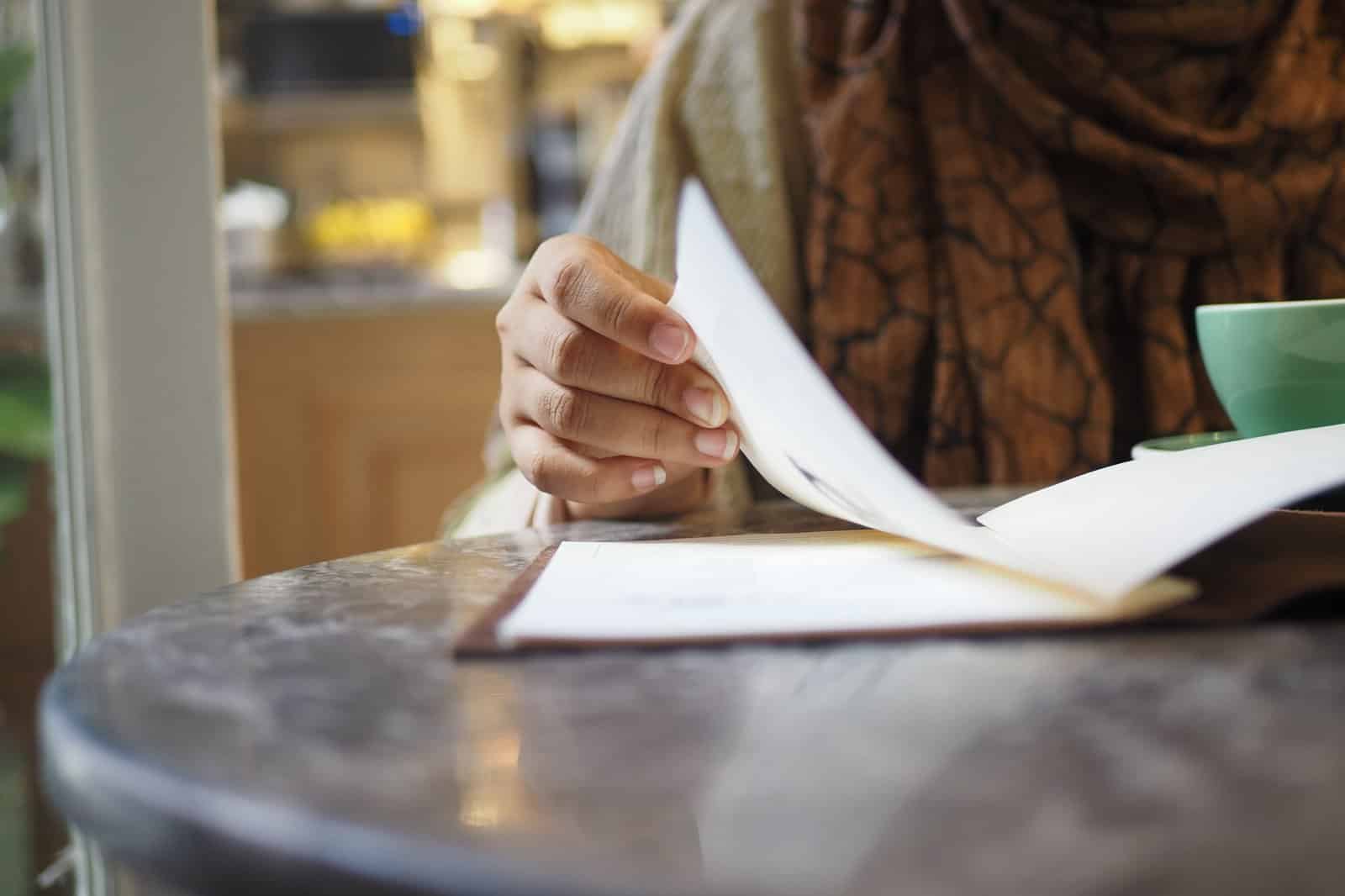 Hand turning the page of a written headache diary at a cafe table