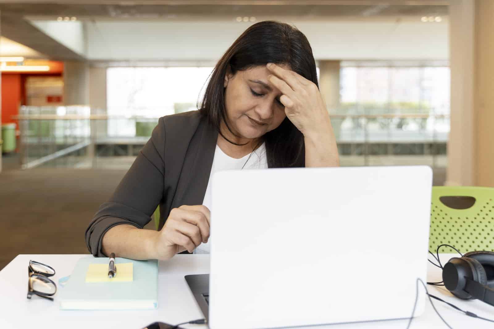 Woman at her office desk holding her forehead in pain from a tension headache