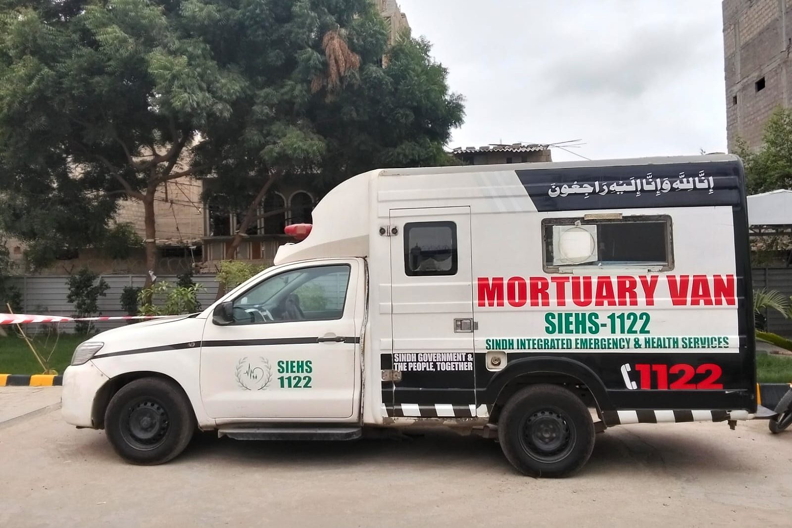 Side view of a free SIEHS 1122 mortuary van in Sindh, with MORTUARY VAN in red, SIEHS-1122 in green, and the 1122 helpline along the side of the body.