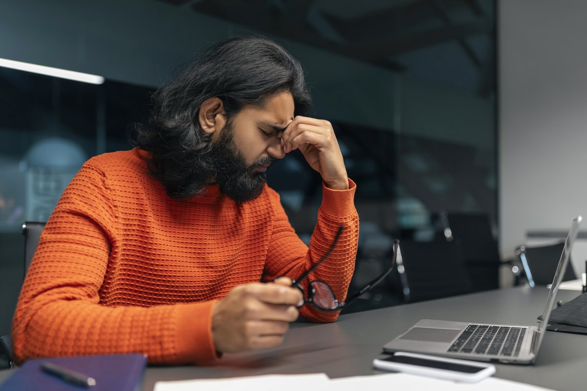 Man at an office desk pinching the bridge of his nose as anxiety triggers a physical stress response