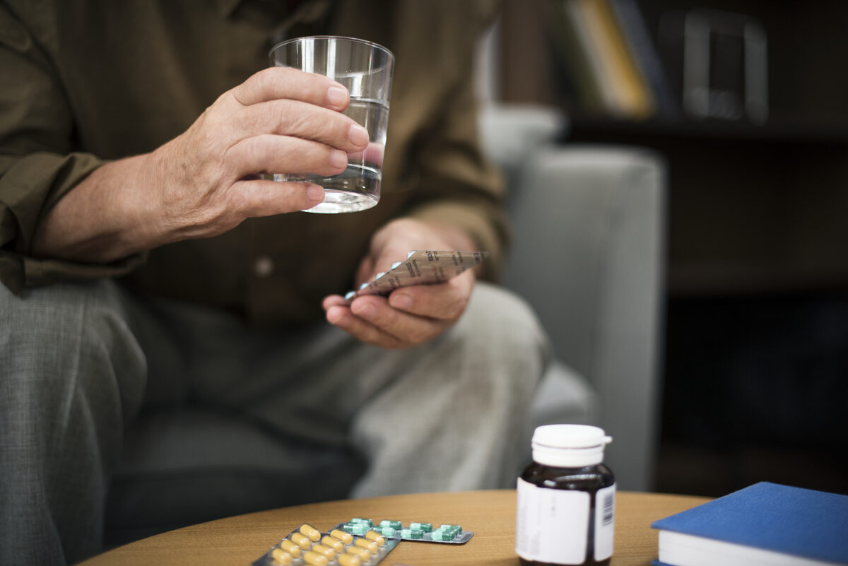 Hands holding medication pills and a glass of water for daily blood pressure treatment