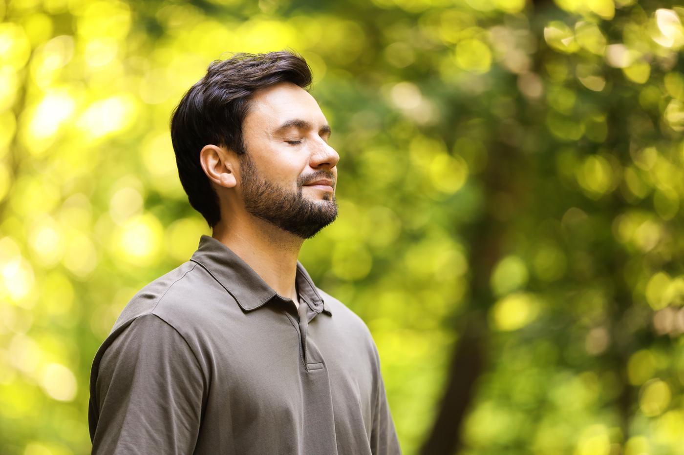 Man standing outdoors with his eyes closed, taking slow, calming breaths
