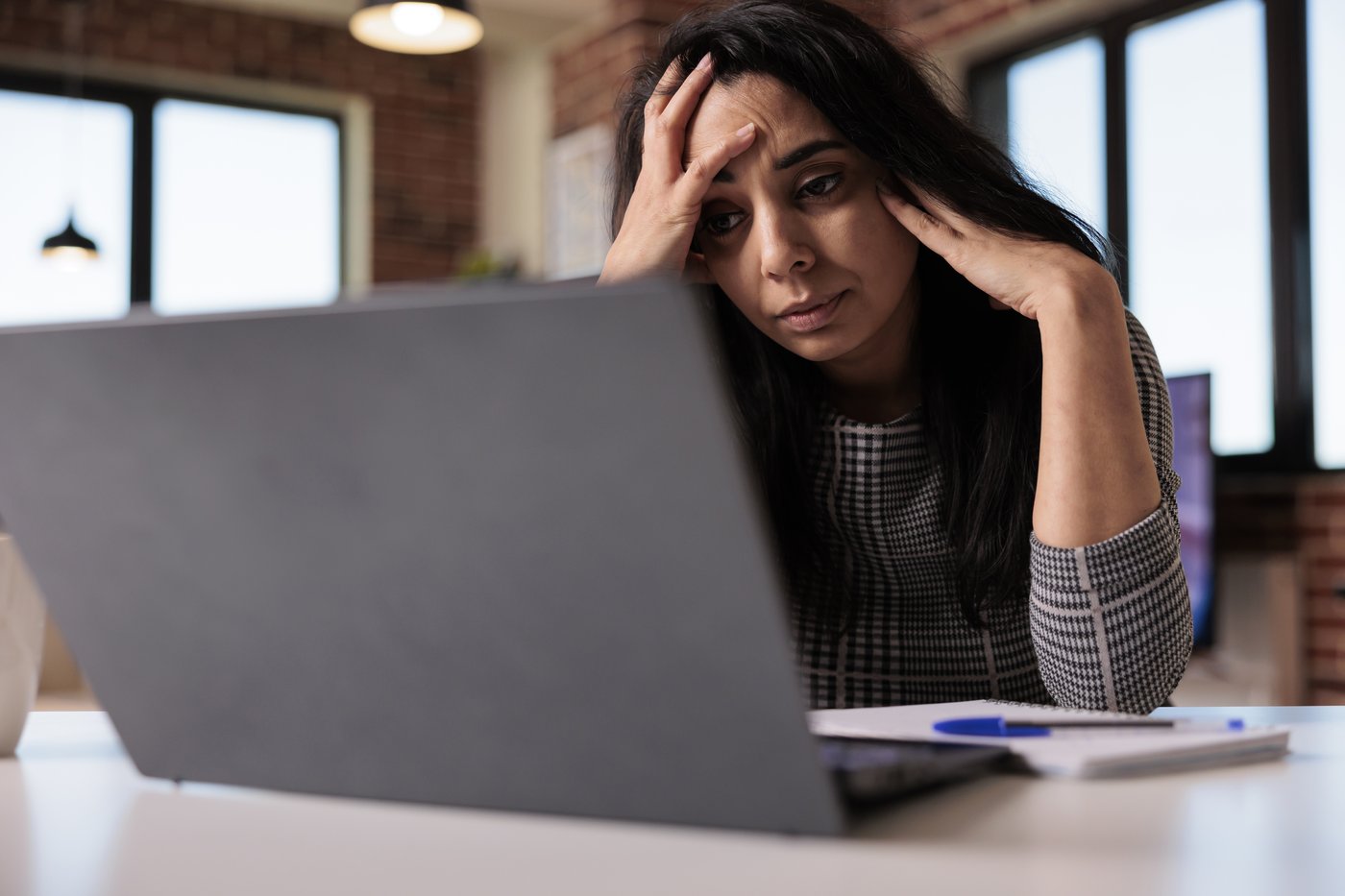 Stressed woman with her head in her hands at her laptop, a common panic attack trigger