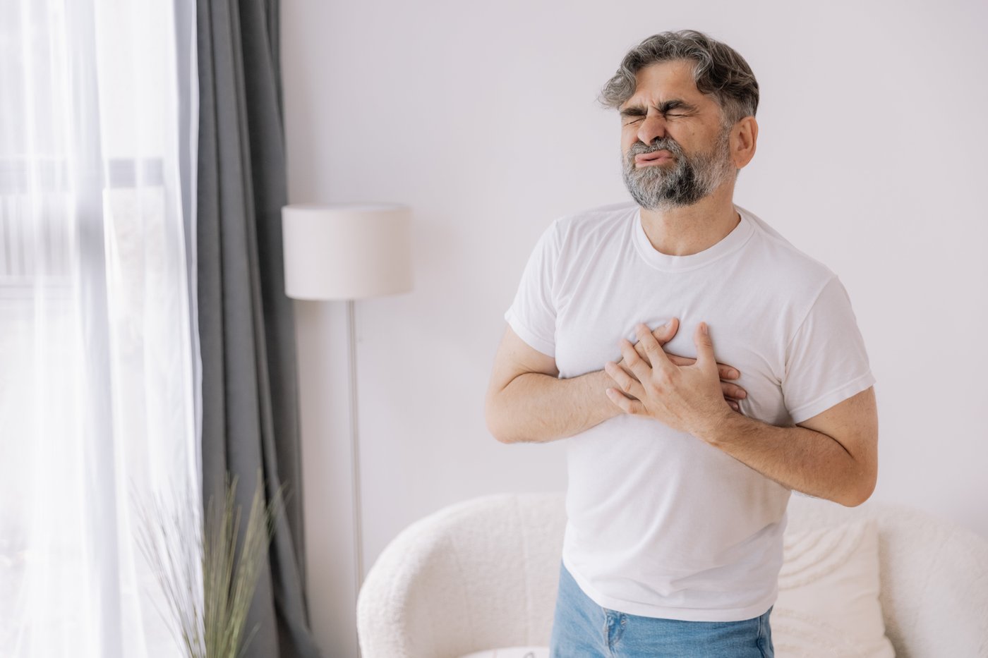 Man with his eyes closed clutching his chest in discomfort at home