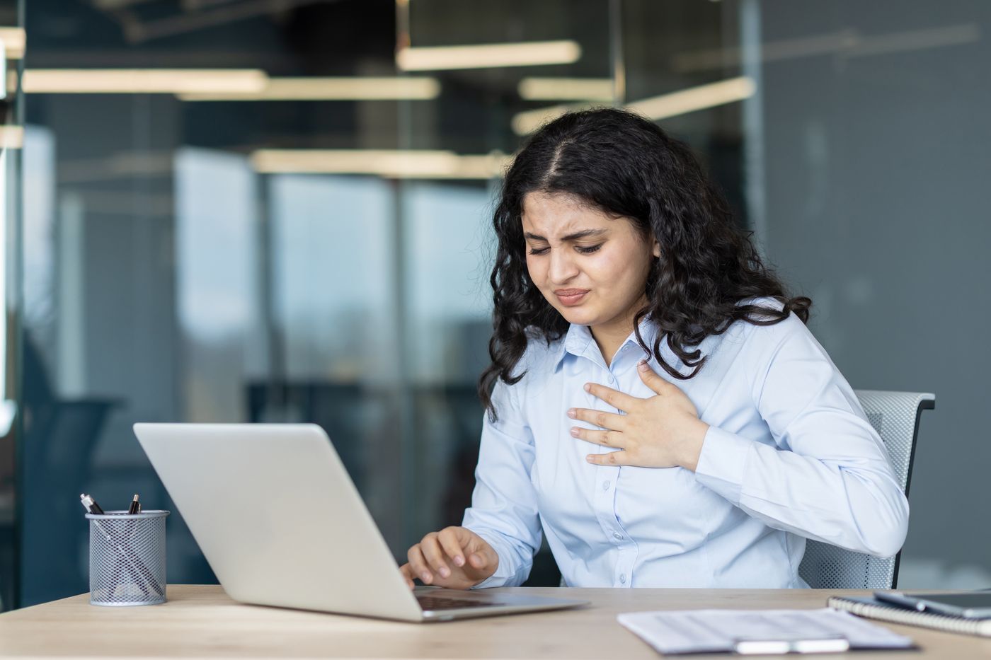 Woman at her office desk with her hand on her chest, showing signs of chest pain and discomfort