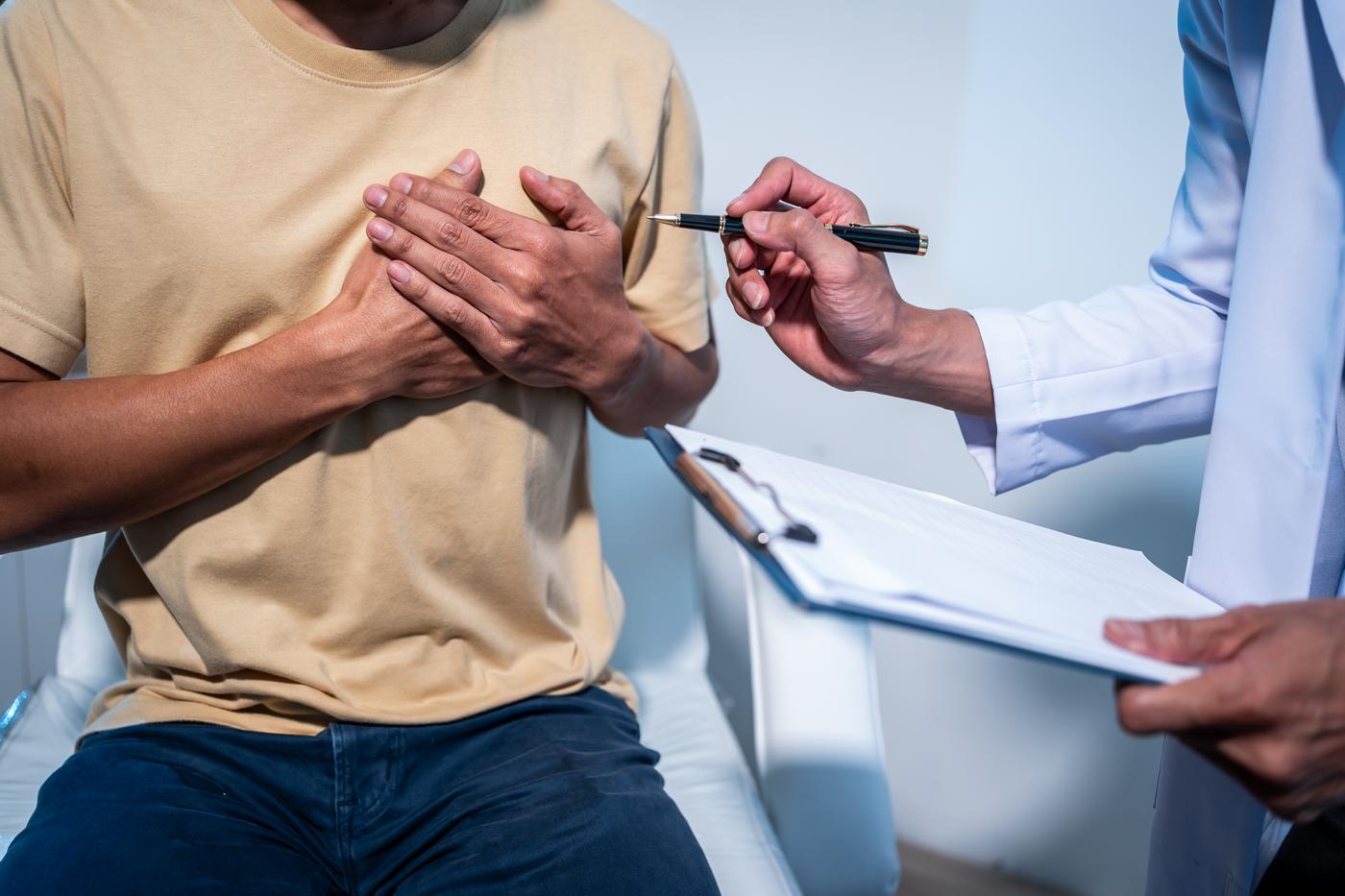 Doctor with a clipboard consulting a patient who has his hand on his chest
