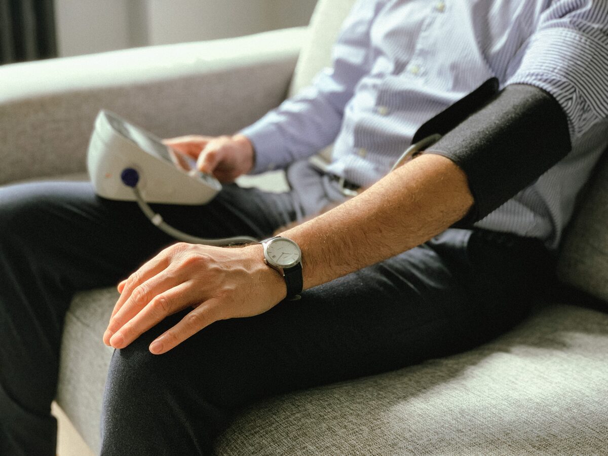 Man checking his own blood pressure at home using an upper-arm monitor on the couch