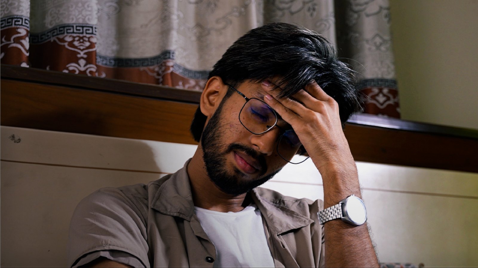 Young man at home holding his head with a headache, wondering who to ask for medical advice