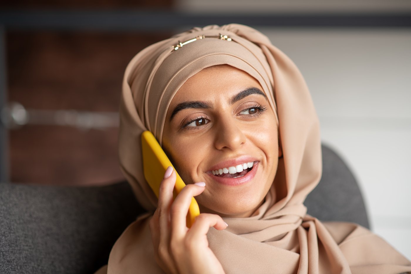 Woman in a hijab smiling while talking on the phone, calling Tele-Tabeeb 1123 for a telemedicine consultation