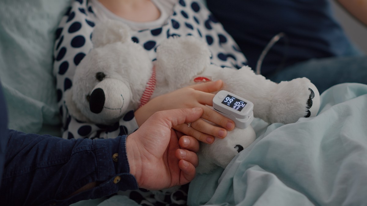 Parent holding a child's hand with a pulse oximeter clipped to the finger