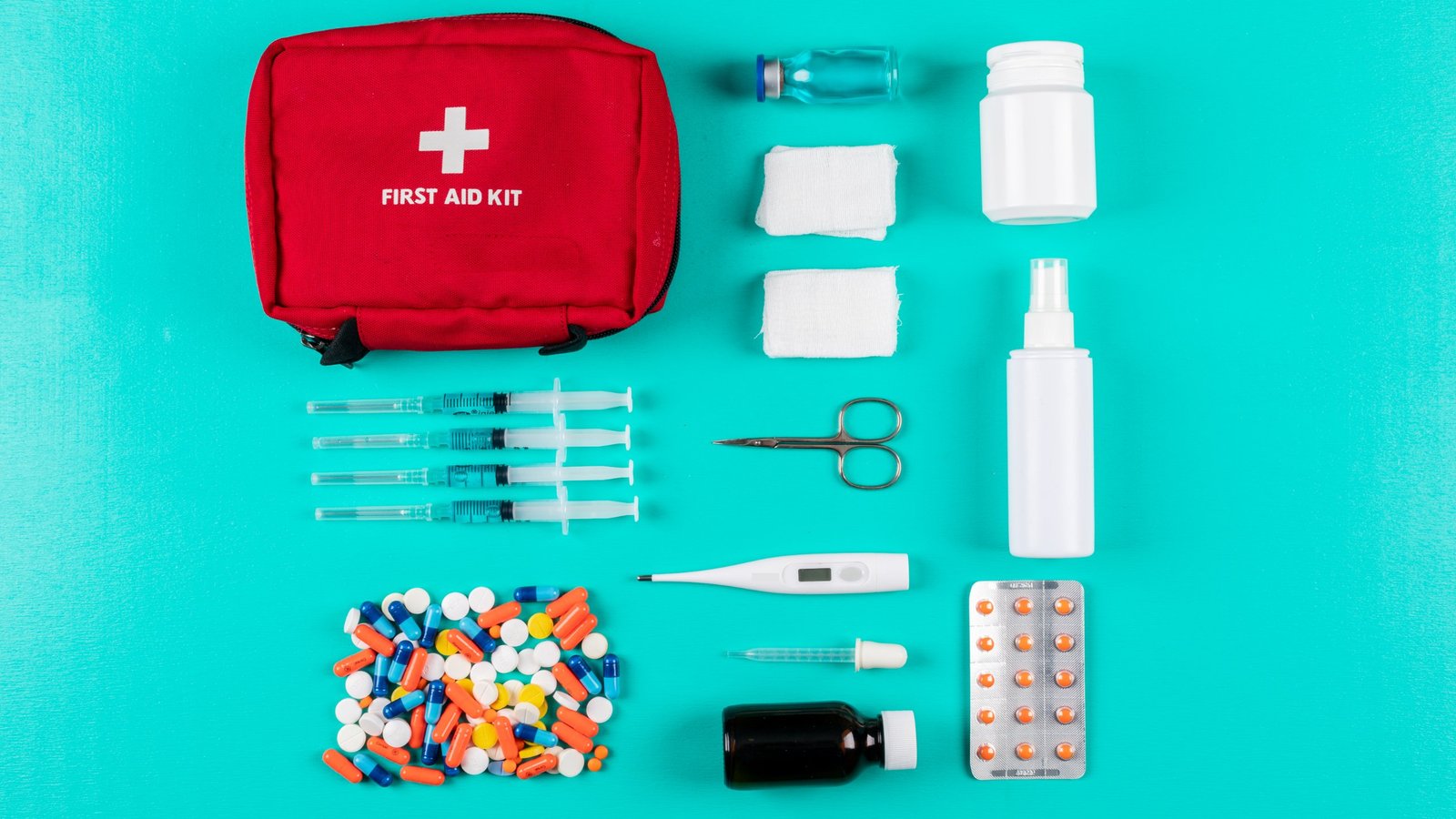 Red first aid kit bag laid out with gauze, scissors, thermometer and medicines for a home and office first aid kit checklist