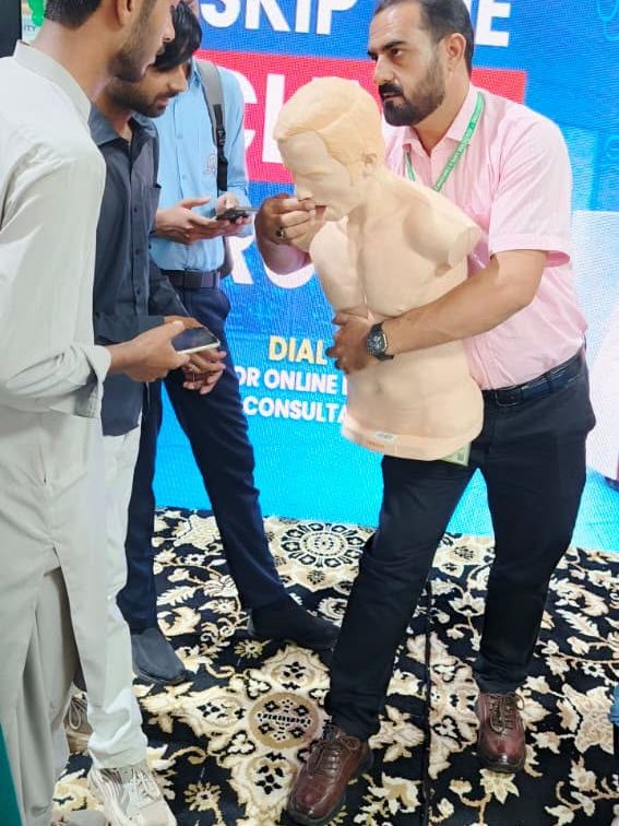Visitors watching a first aid demonstration with a training manikin at a health expo stand