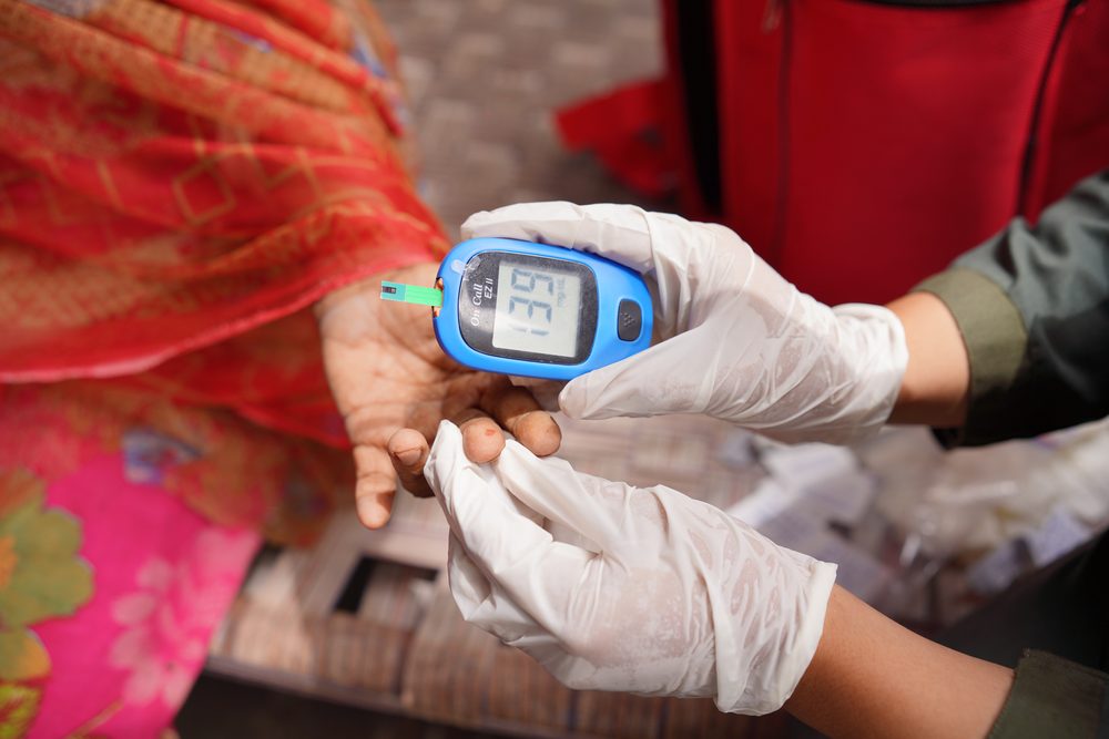 Gloved hands holding a glucometer that shows a single blood sugar reading