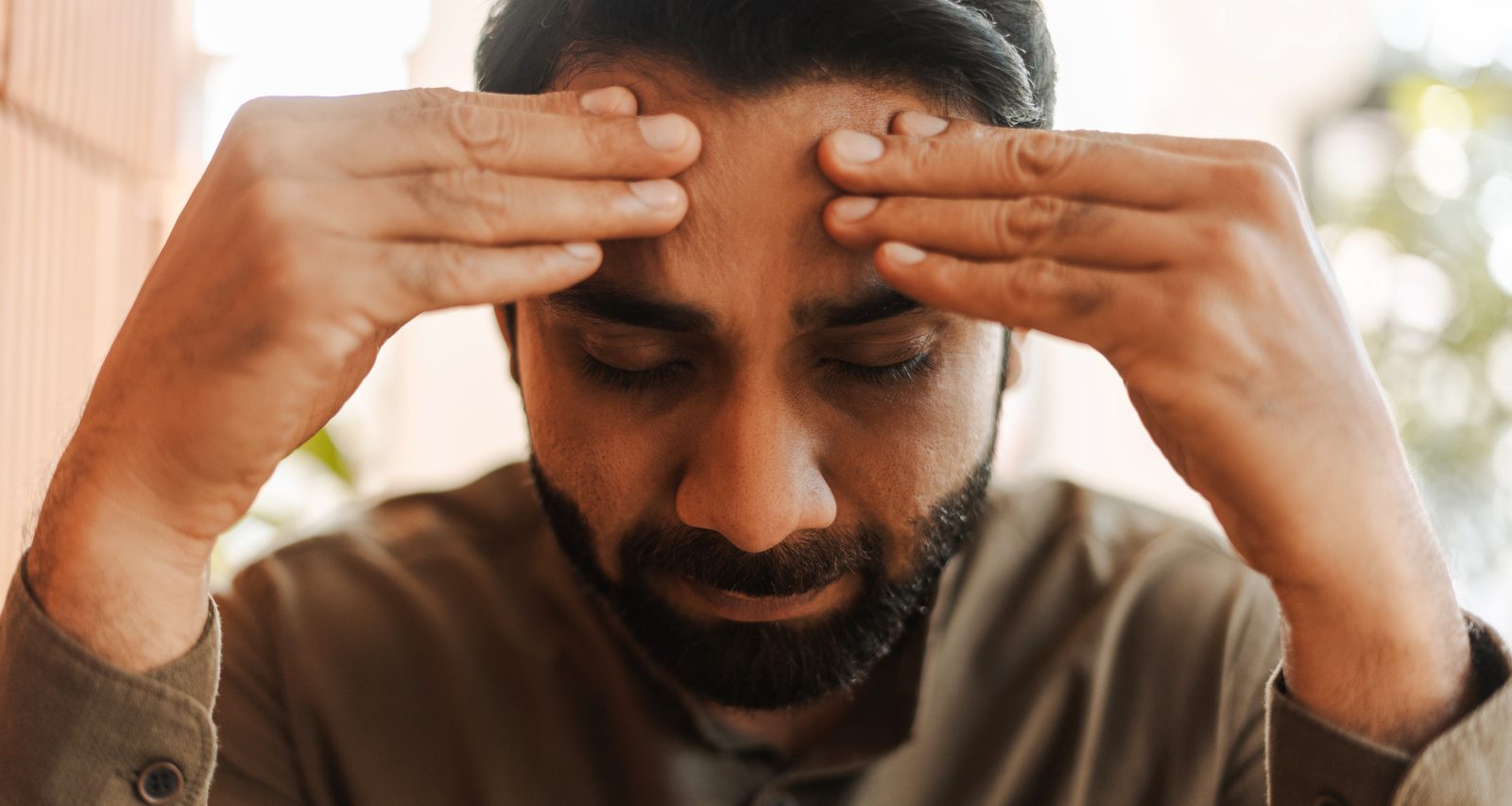 Man with eyes closed pressing his temples, showing the dizziness and headache that can come with low blood sugar
