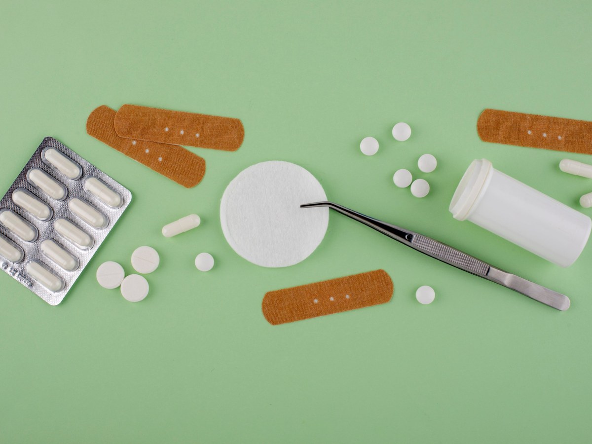 Plasters, a cotton pad, tweezers and tablets arranged on a green background for an office first aid box