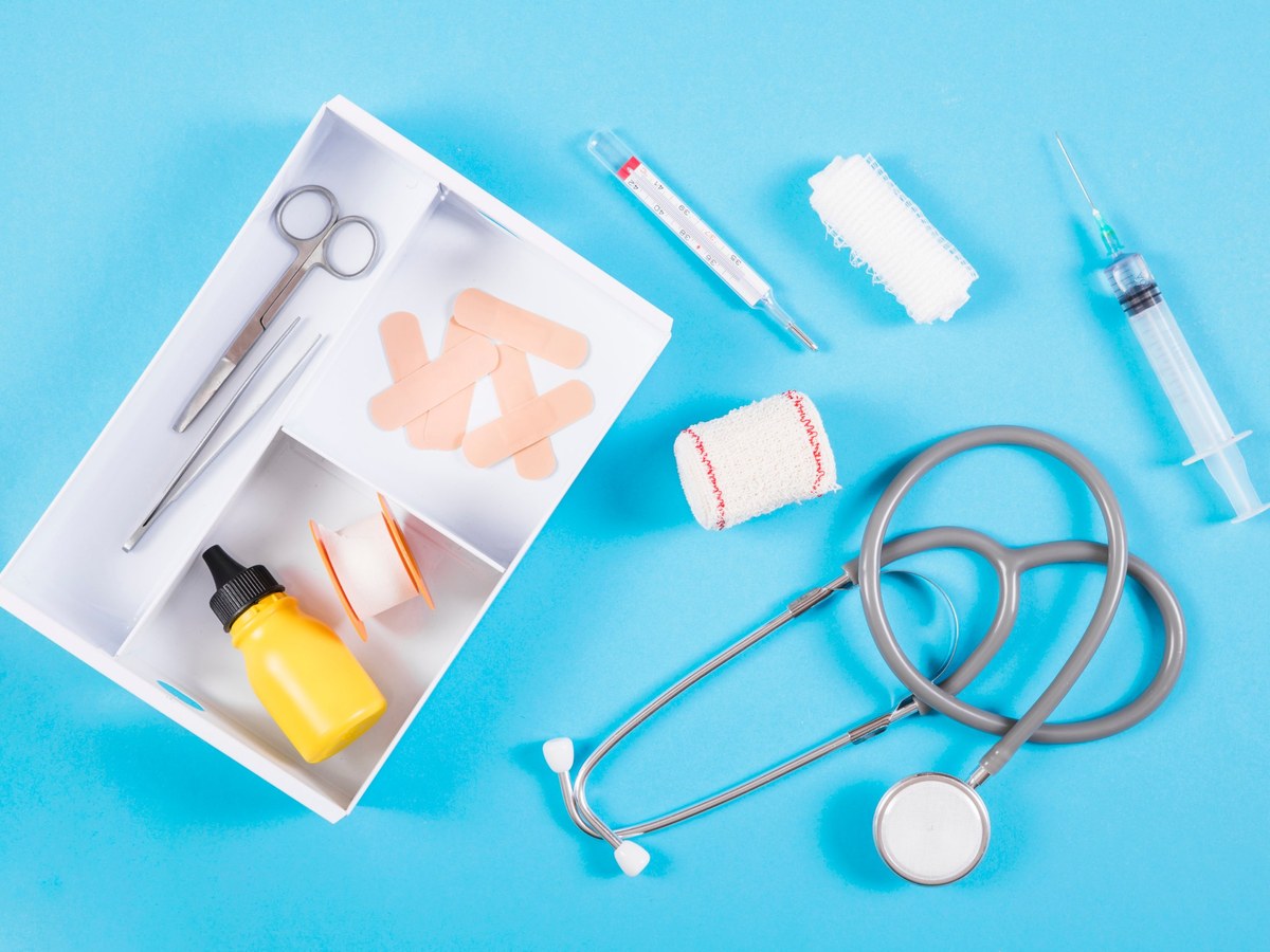 First aid supplies including scissors, tweezers, plasters, tape, a thermometer and gauze arranged on a blue background