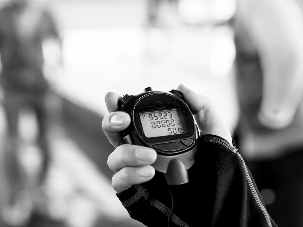 A hand holding a digital stopwatch, shown in black and white