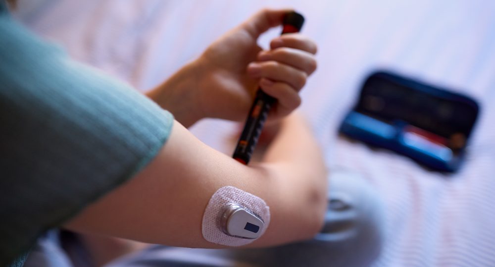 Person injecting insulin with a pen while wearing a glucose sensor on the upper arm