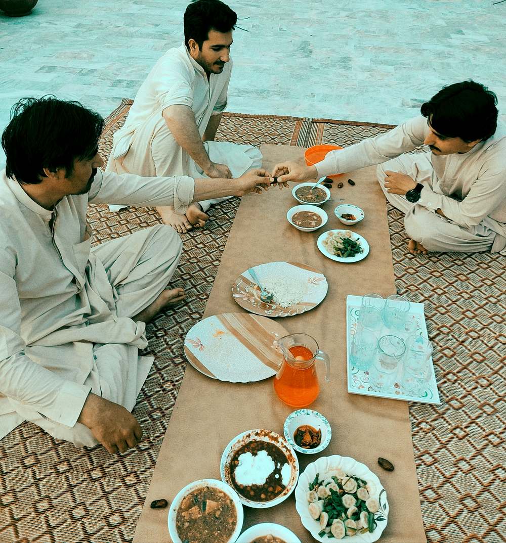 Men sharing dates, water and iftar dishes on a mat while breaking a fast