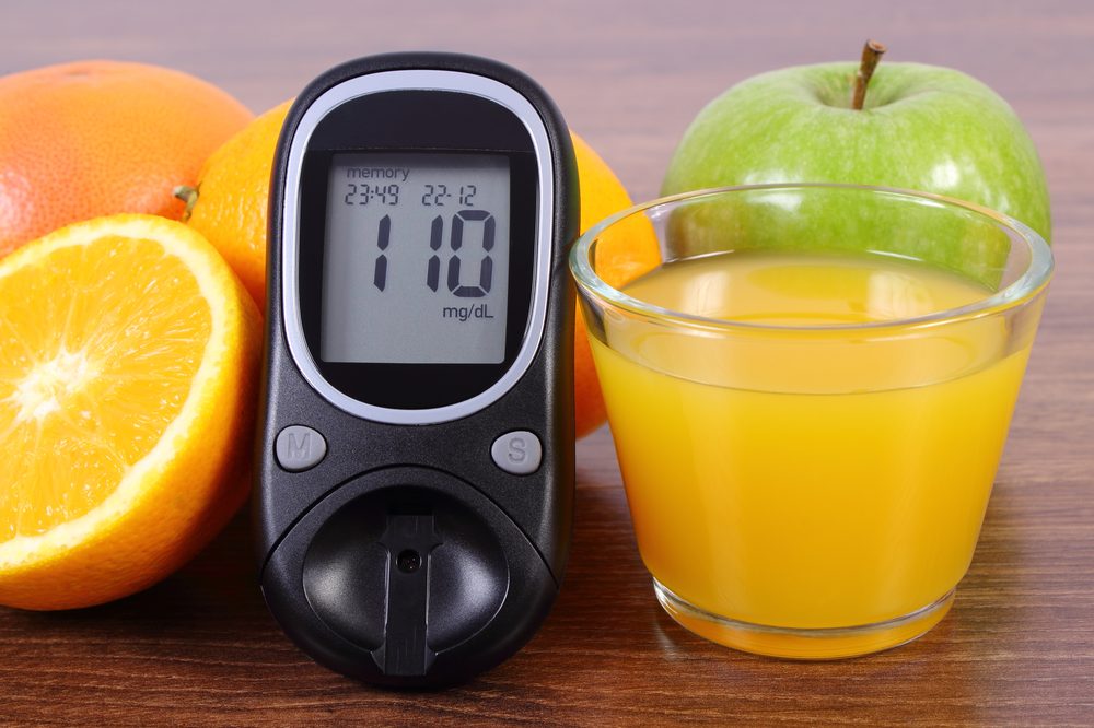 Glucose meter beside a glass of orange juice and fresh fruit, a quick-acting sugar source for a low